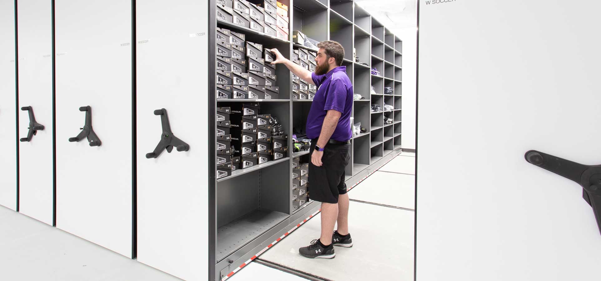 big 10 football team gear storage on high-density mobile system with staff member retrieving what's needed