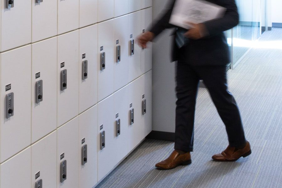 Office employee in a suit walking past a wall of day use lockers towards break room with couch