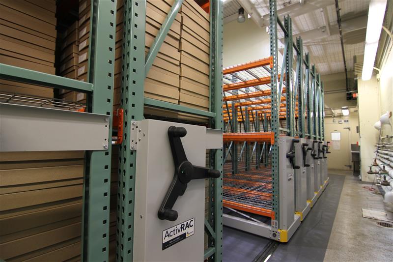 Mechanical assist mobile racking system holding many boxes in a warehouse