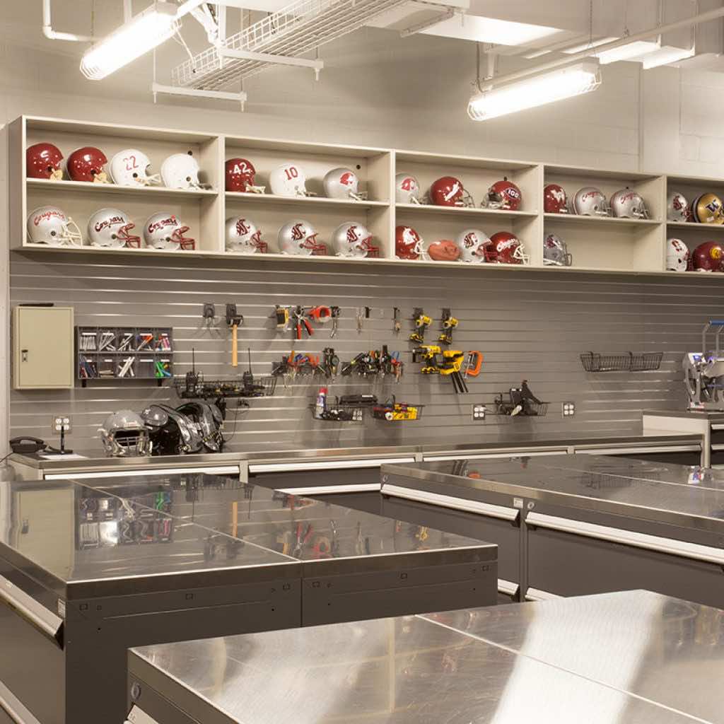 stainless steel countertops for gear repair in a football equipment room with shelves holding helmets in the background