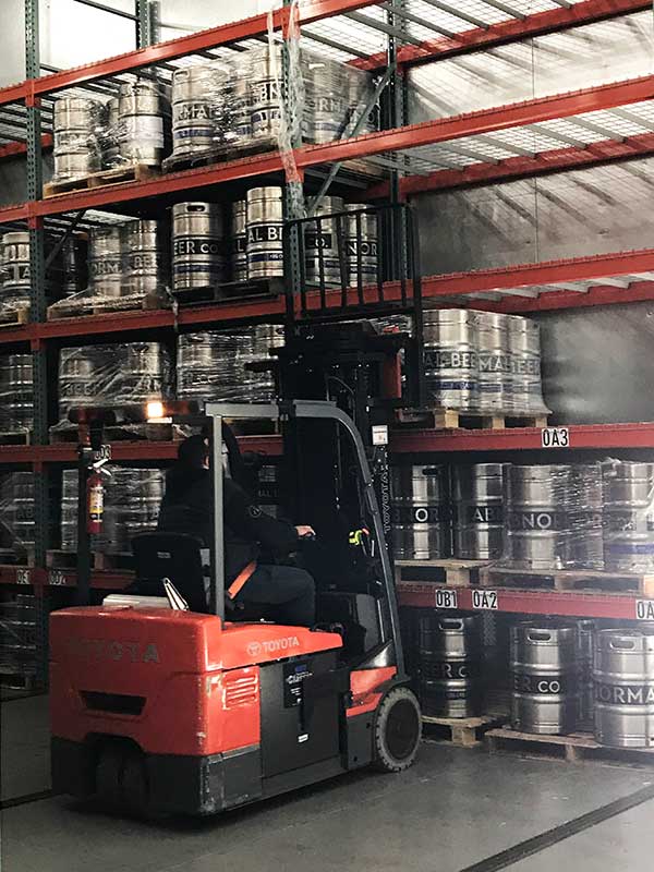fork lift lifting a pallet of beer kegs off of a mobile shelving system