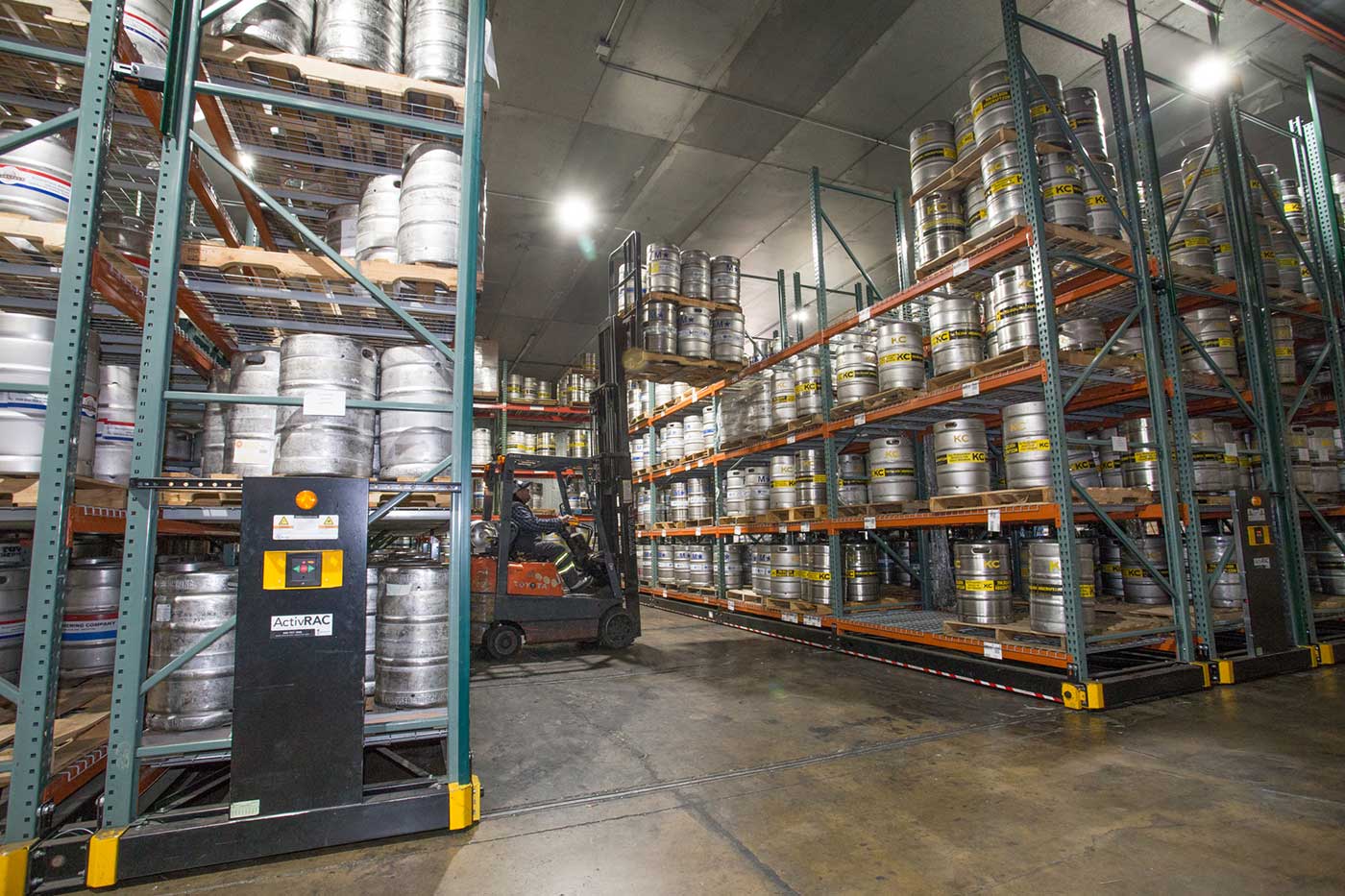 Powered mobile racking system holding beer kegs with a forklift lowering a pallet of kegs