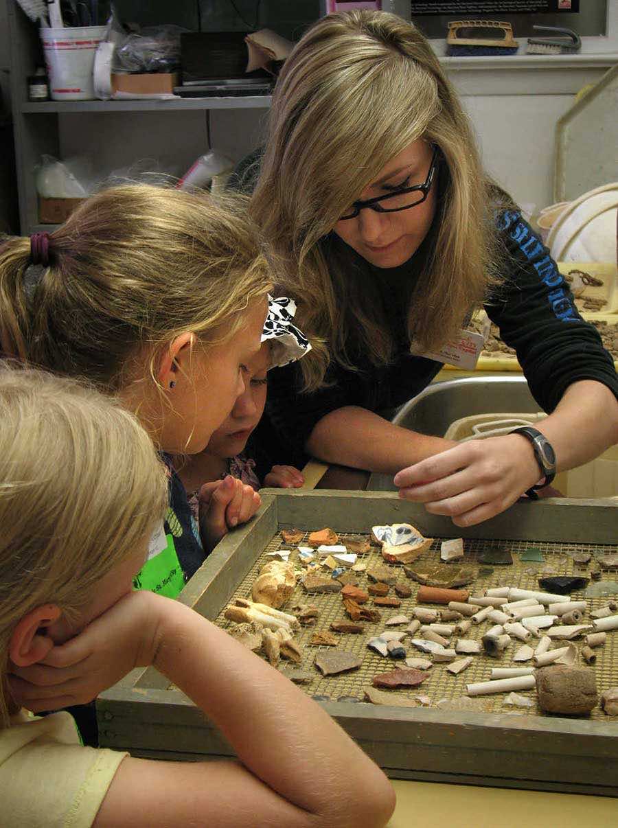 Museum curator showing collection of artifacts to children