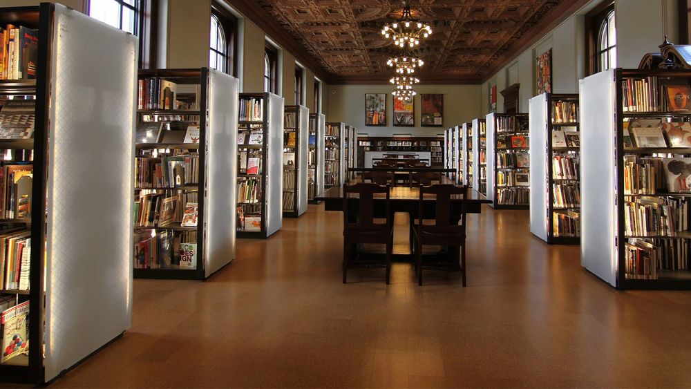 Spacesaver illuminated library shelving in large library room with tables and chandelier