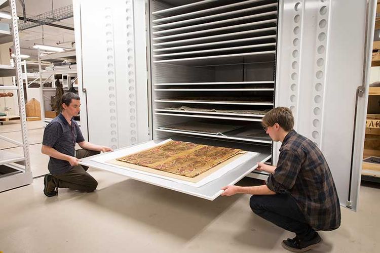 Oversize museum cabinet with two people holding a tray protecting an artifact 