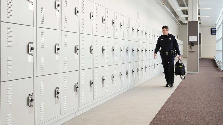 police officer carrying a duty bag walking along a wall of duty bag lockers