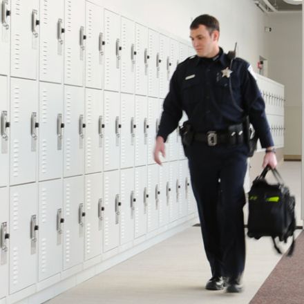 police officer with duty bag walking past a wall of white duty bag lockers