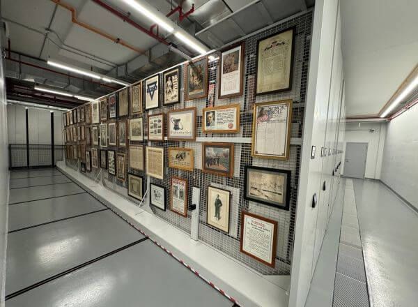 Various framed military posters and documents displayed on a Spacesaver mobile art rack