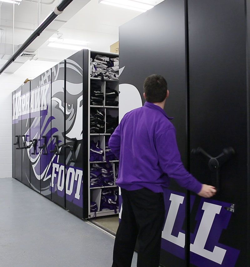 Football equipment room staff member turning high-density mobile system wheel to move stacks