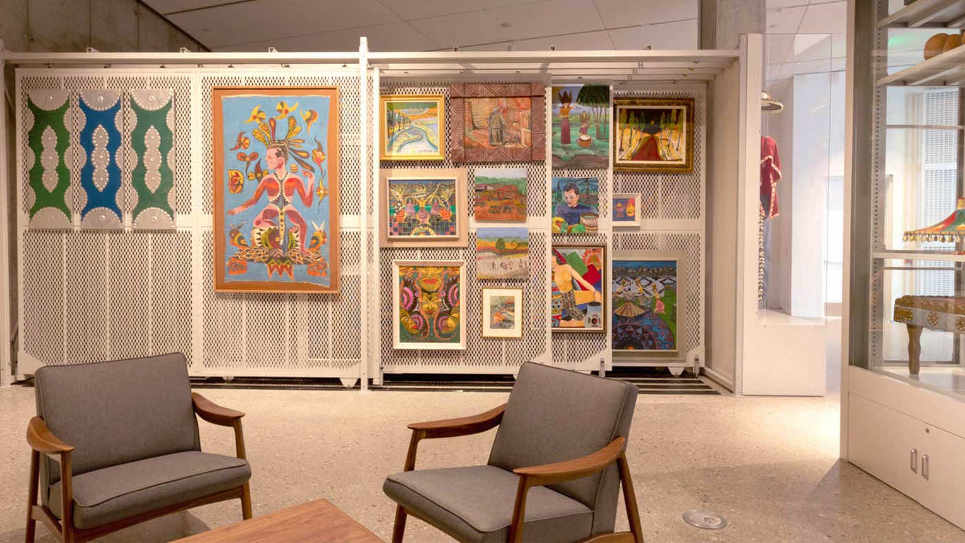 museum collection paintings on hanging art racks with two chairs and a small table nearby