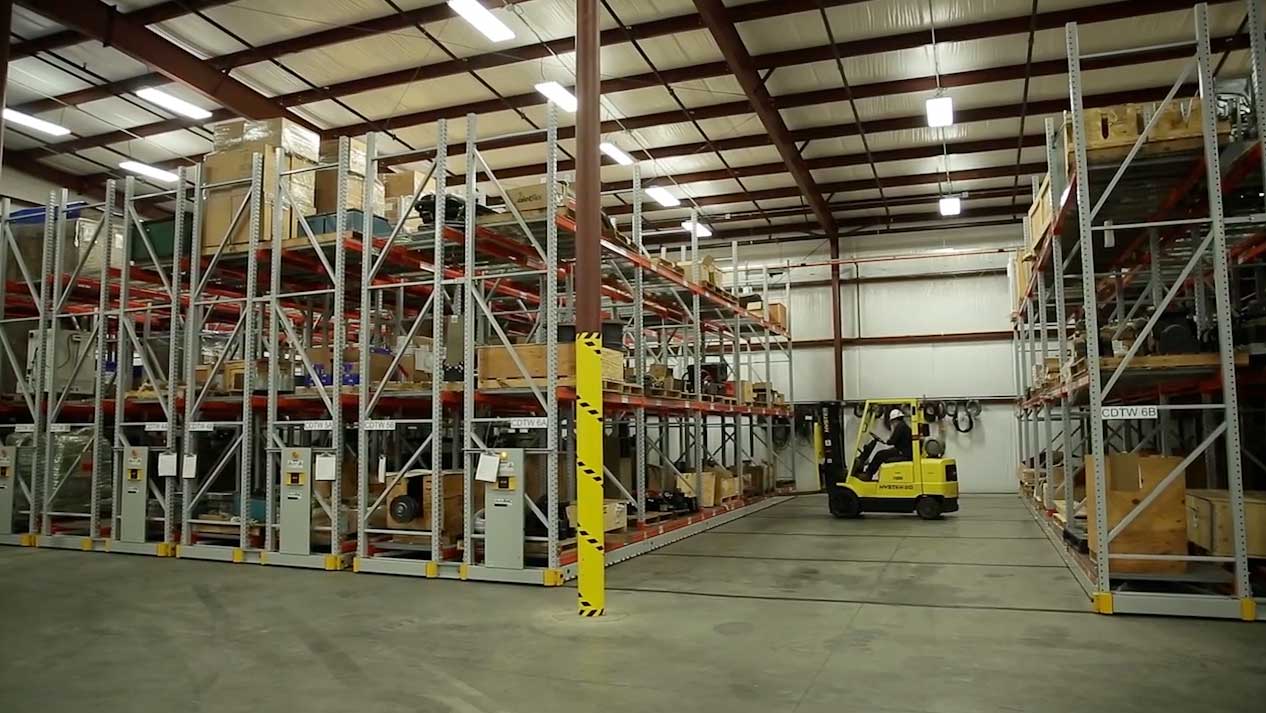 A powered mobile racking system with a forklift about to pick something up off of it